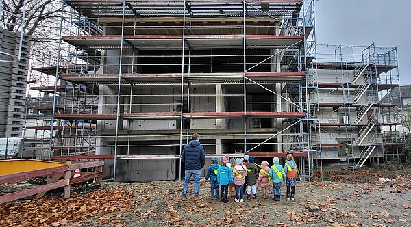 Kinder stehen vor Baugerüst und schauen auf eine Baustelle