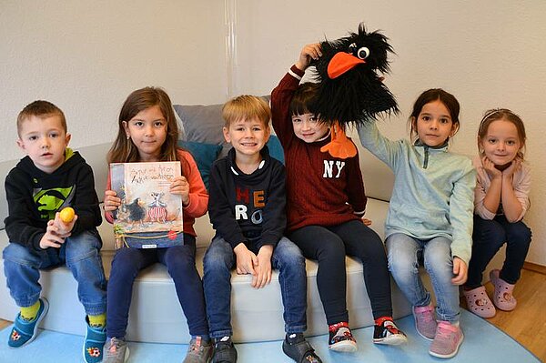 Die KiTa-Kinder halten ein Ei, das vorgelesene das Buch und den Raben Anthon in der Hand