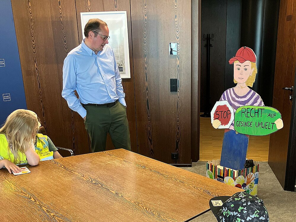 Die Kinder pr&auml;sentieren Thomas Kufen ihre selbstgestaltete Pappfigur, die Besucher*innen &lrm;des Rathauses auf das Recht auf eine gesunde Umwelt hinweisen soll. &lrm;