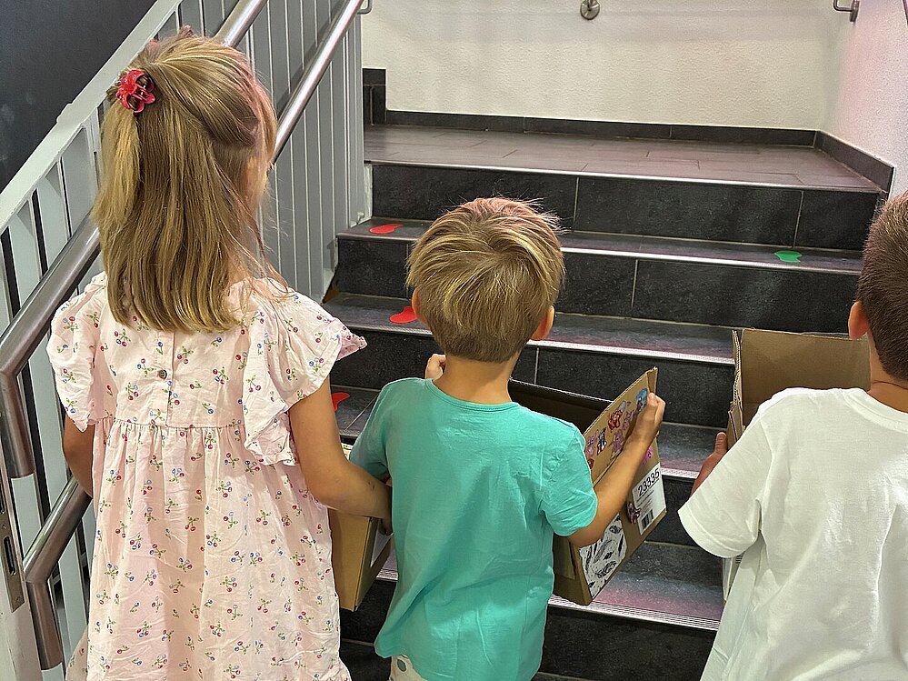 Kinder tragen Umzugskartons durch die KiTa