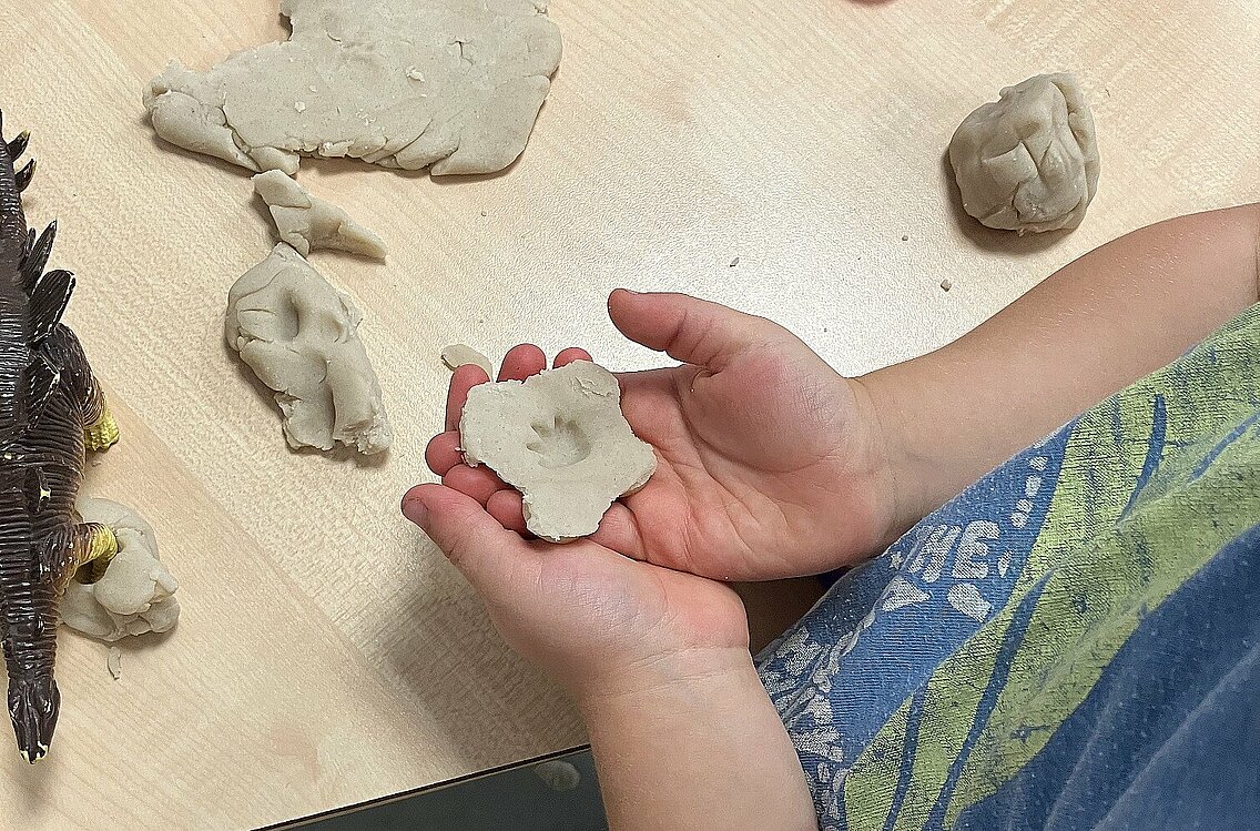 Kind hält Knete mit Dino-Fußspur in den Händen