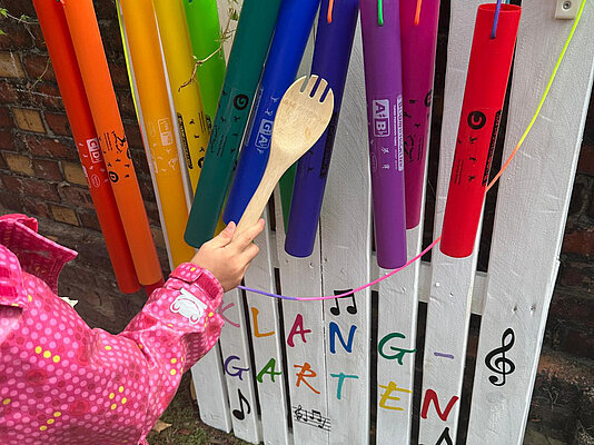 Kind musiziert mit Holzlöffel und Plastikrohren