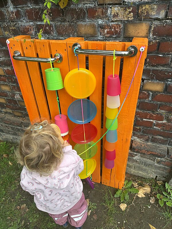 Kind musiziert mit Holzlöffel und Plastikrohren
