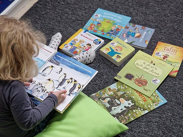 Kind sitzt auf dem Boden und schaut sich Bücher an