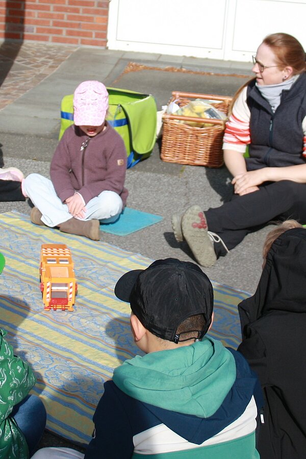 Kinder sitzen um ein Spielzeug-Müllauto