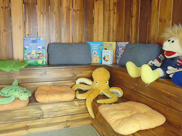 Eingerichtete Holz-Lounge mit Kuscheltieren und B&uuml;chern