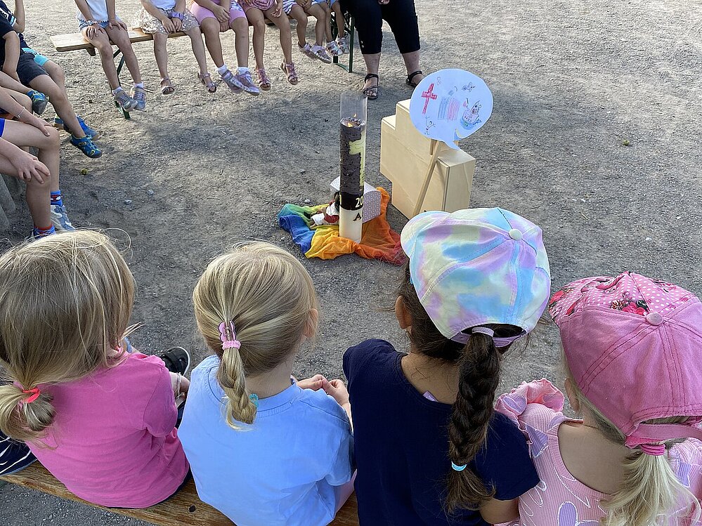 Kinder sitzen im Kreis um ein religionspädagogisches Bodenbild mit Kreuzkoffer
