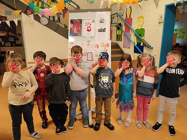 Kinder halten rote Hand vor ihre Gesichter