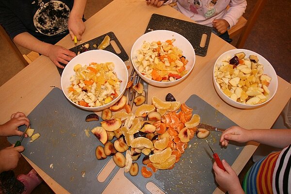Kinder schneiden auf einem Tisch Obst für einen Obstsalat
