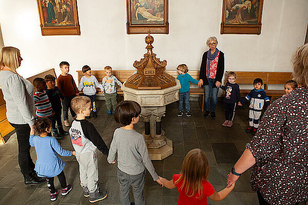 Kinder stehen um Taufbecken in Kirche