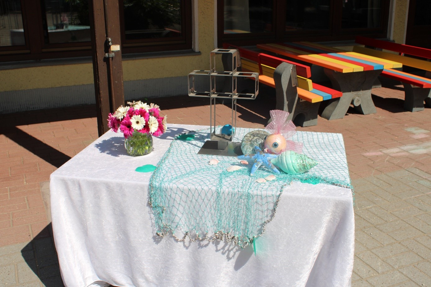 Auf einem Tisch steht ein Blumenstrauß, ein Kreuz und Meeres-Accessoires