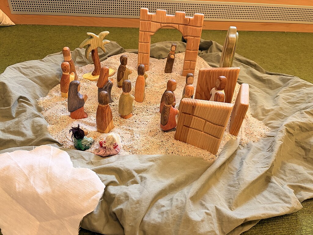 Kinder stellen Pfingstgeschichte mit Holzfiguren im Sand nach